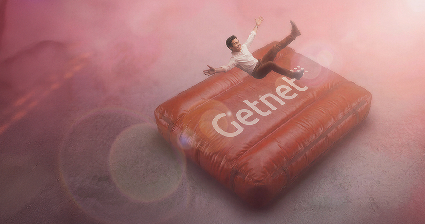 Persona cayendo sobre un colchón inflable rojo con el logo de Getnet, sobre un fondo rosado.