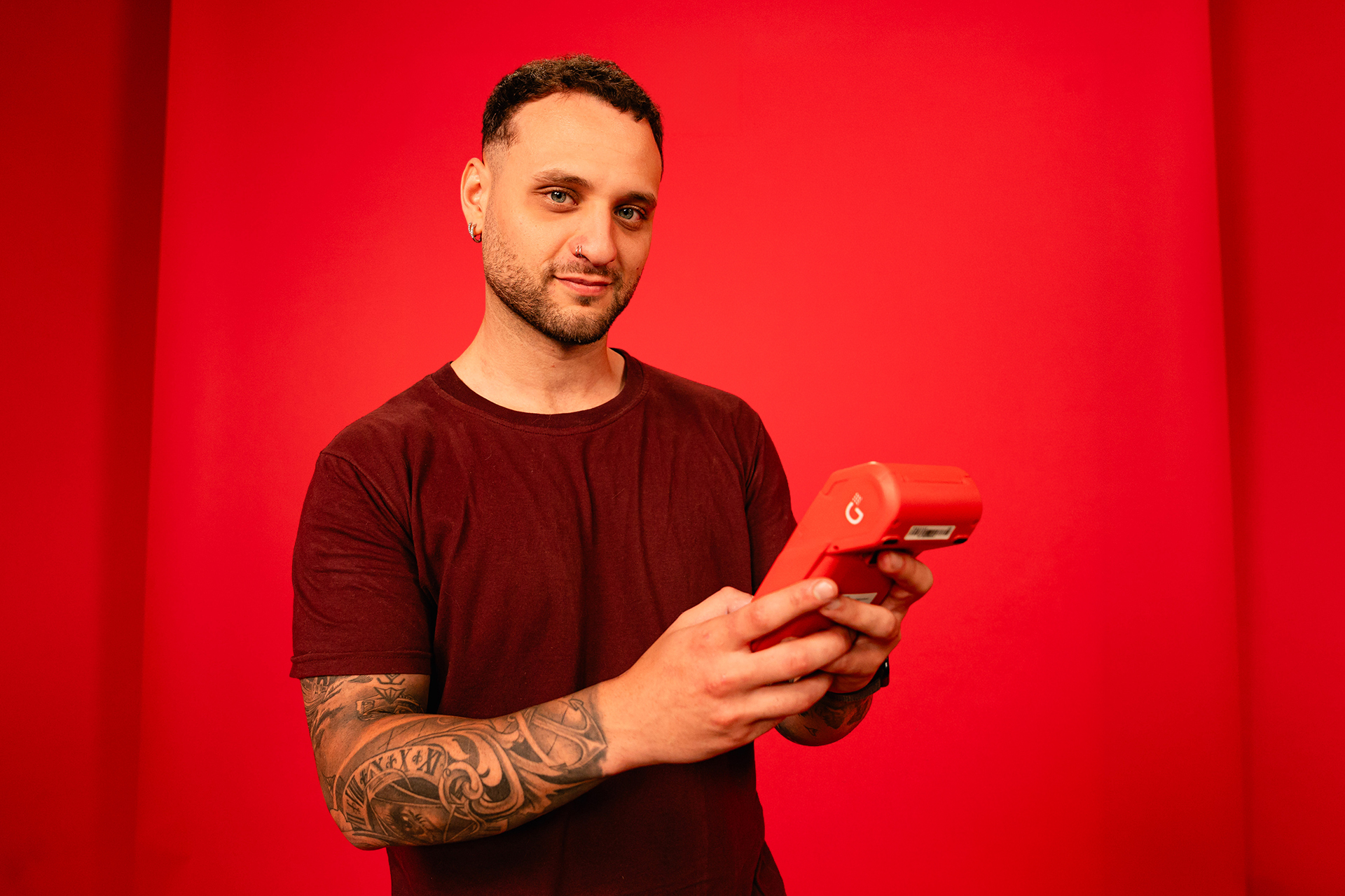 Persona sosteniendo una terminal de cobro roja frente a un fondo rojo.