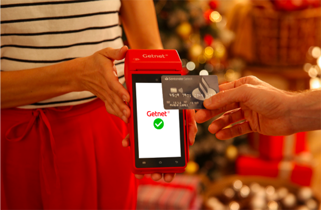 Pago con tarjeta contactless en una terminal de cobro Getnet roja, con pantalla que muestra confirmación de pago, sobre fondo con decoración navideña.